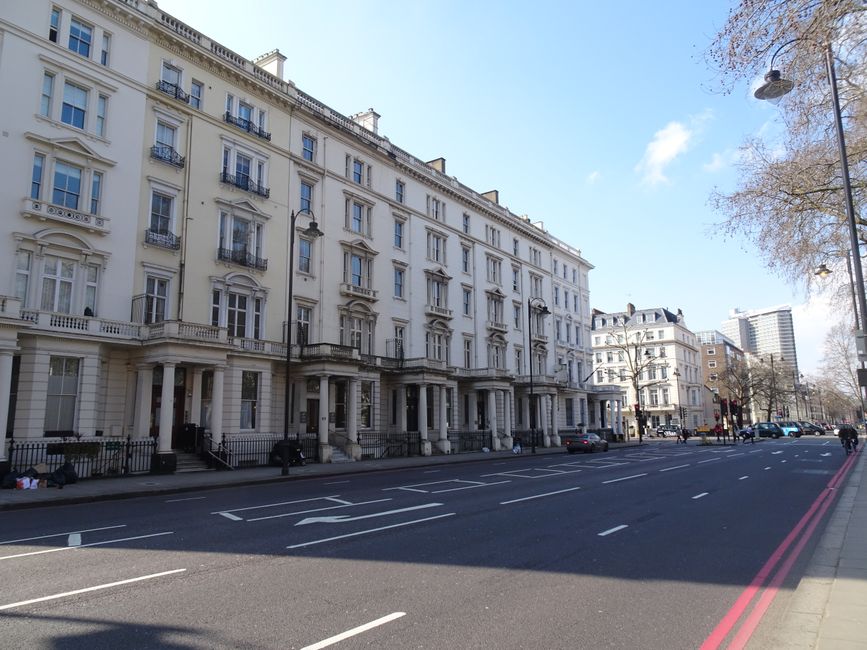 A row of elegant, white Victorian-style terraced buildings with multiple large windows and decorative architectural features, situated along a street with parked cars of various makes and colours. Sev